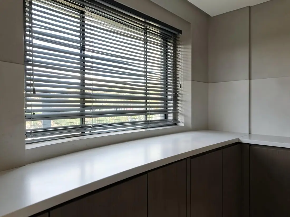 Cozinha contemporânea com persiana de alumínio na janela e bancada limpa, sob luz natural lateral
